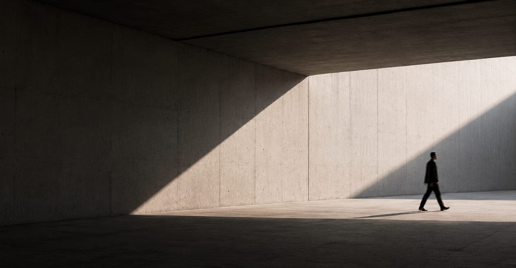 Pessoa caminhando em um espaço de concreto com luz diagonal